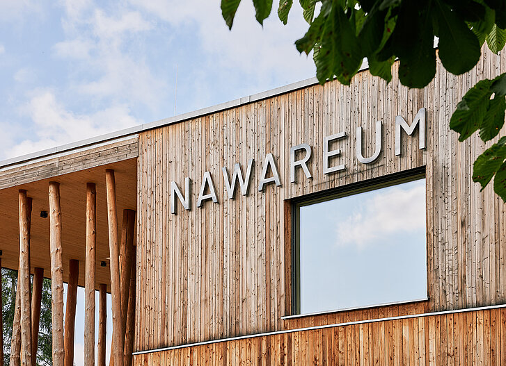 Fokus auf den NAWAREUM-Schriftzug, der mit Stahlbuchstaben auf der Holzfassade des Museums befestigt ist.
