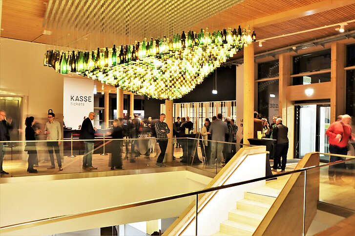 Bei einer Abendveranstaltung im NAWAREUM tummeln sich Menschen im stimmungsvoll beleuchteten Foyer.