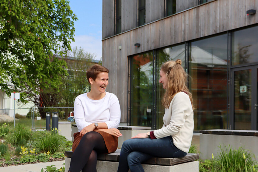 Zwei Frauen unterhalten sich lachend auf einer Bank im Garten NAWAREUMs.